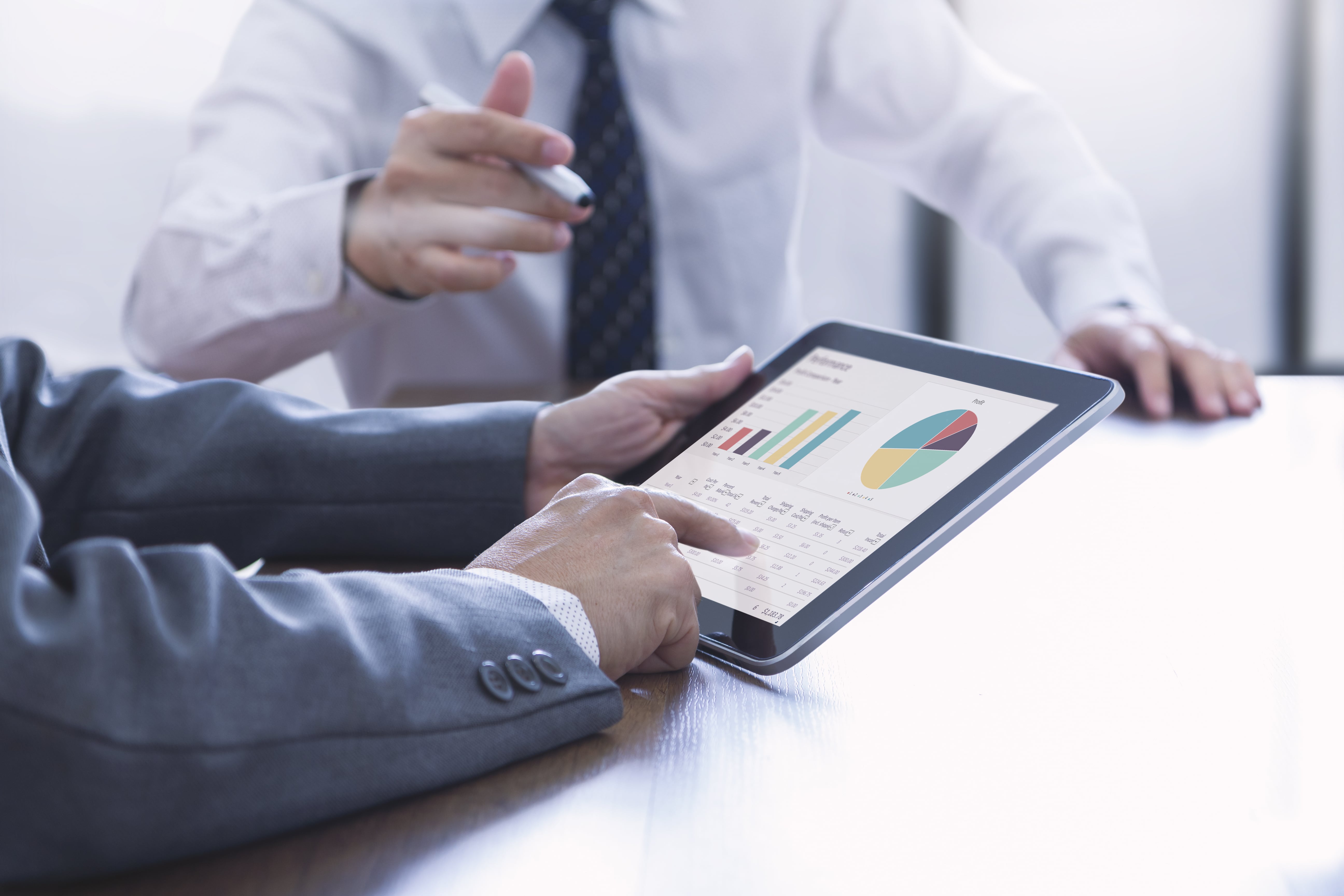 two-business-men-meeting-room-discuss-financial-performance-investment-analysis-with-worksheets-charts-tablet-screen-min